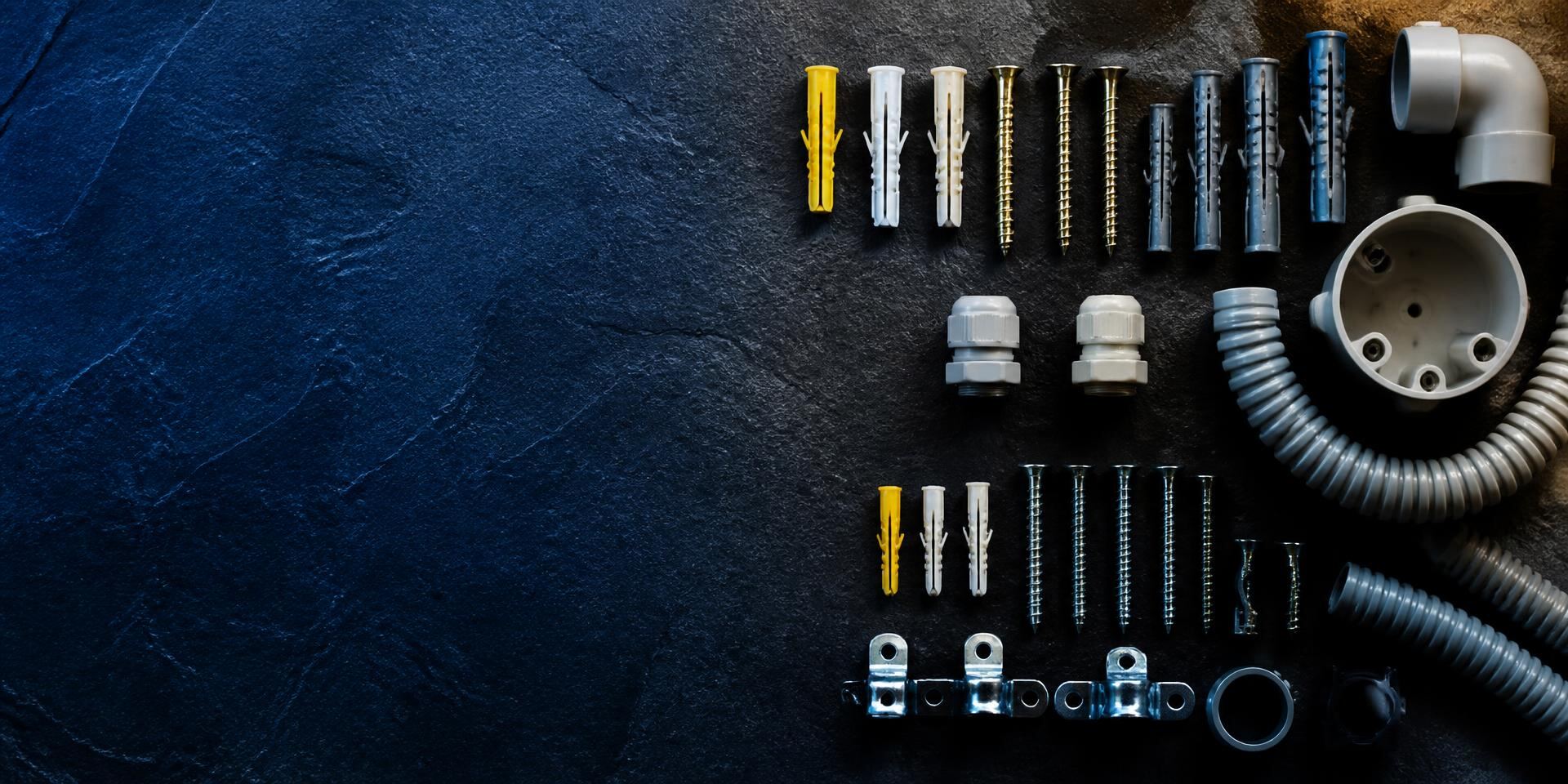 Assorted plastic wall plugs, screws and conduit fittings laid out on a dark surface